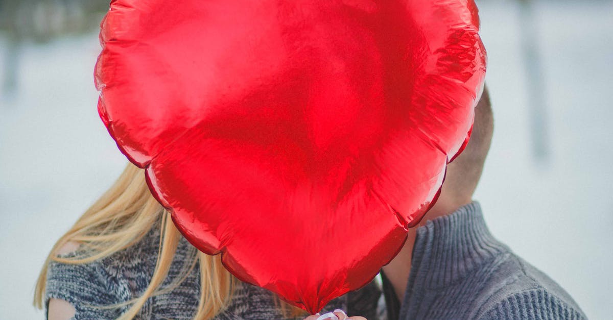 A couple embraces behind a heart-shaped balloon outdoors, depicting love and romance.