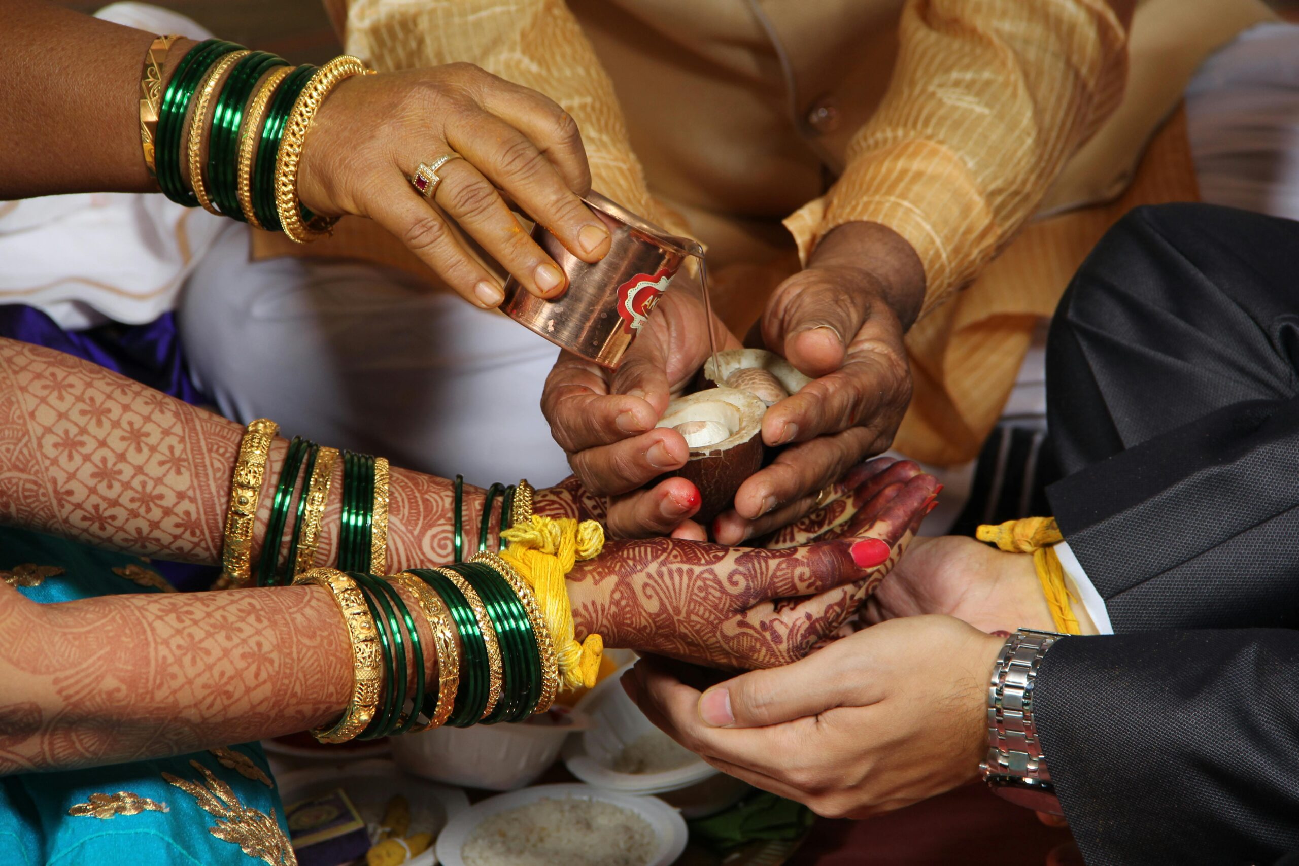 Close-up of a Hindu wedding ceremony showing hands adorned with henna and traditional jewelry.