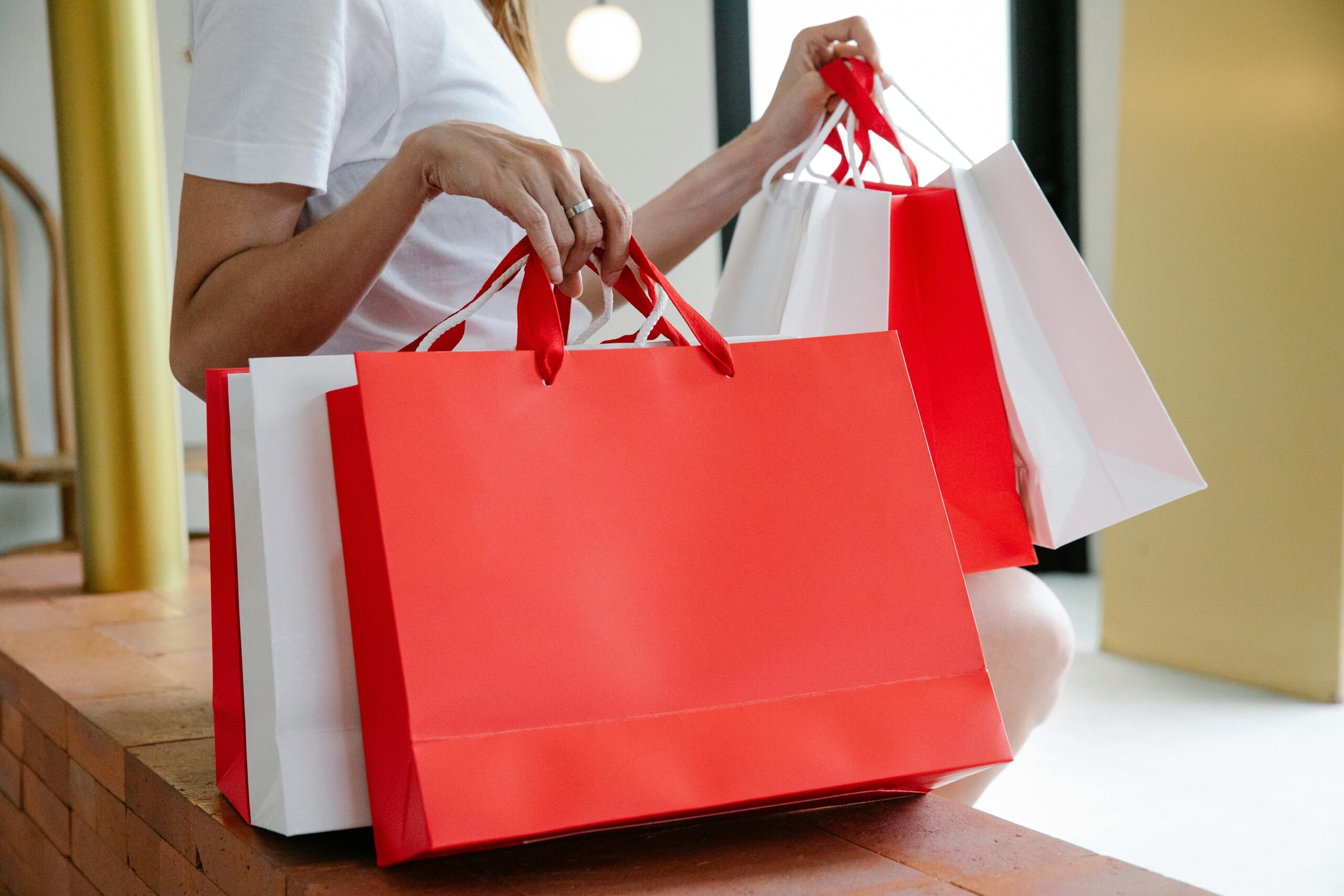 Side view of crop anonymous female buyer in white t shirt sitting on bench with many shopping bags in daylight